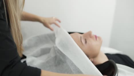 Hairdresser-wrapping-woman's-hair-in-white-towel-after-washing-before-haircut-above-the-sink-in-a-beauty-saloon.-Lady-in-barbershop-beauty-saloon.-Preparing-for-style-haircut