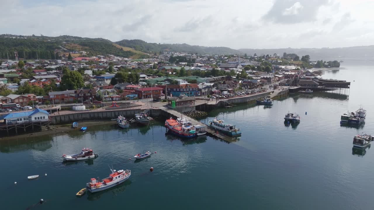 Aerial view of Dalcahue's harbor, town, and surrounding scenic environment. Dolly Back, Rising Shot