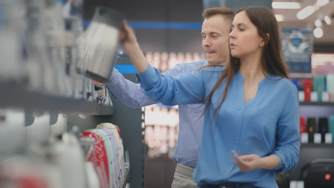Couple man and woman choose electric kettle in the store