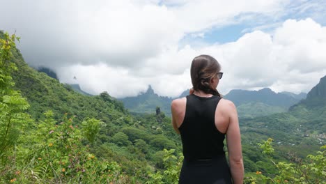 young caucasian woman with sunglasses looking at a mountains on a sunny day in a tropical island with mountains in background in mouaputa, moorea, french polynesia.