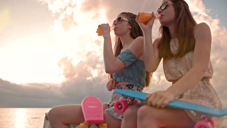 teenage friends with skateboards drinking soda at beach at sunset