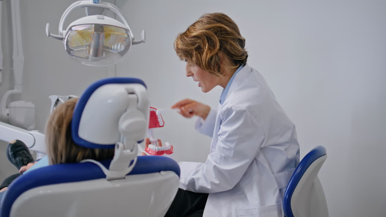 Doctor teaching oral hygiene to child patient in clinic closeup. Woman dentist