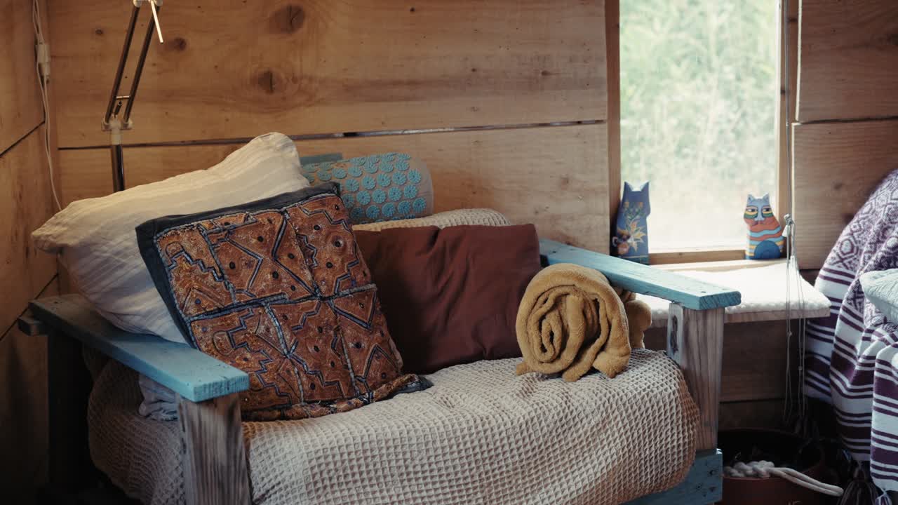 Cozy chair with rustic wooden walls, colorful pillows, and natural light, symbolizing tranquility and warmth.