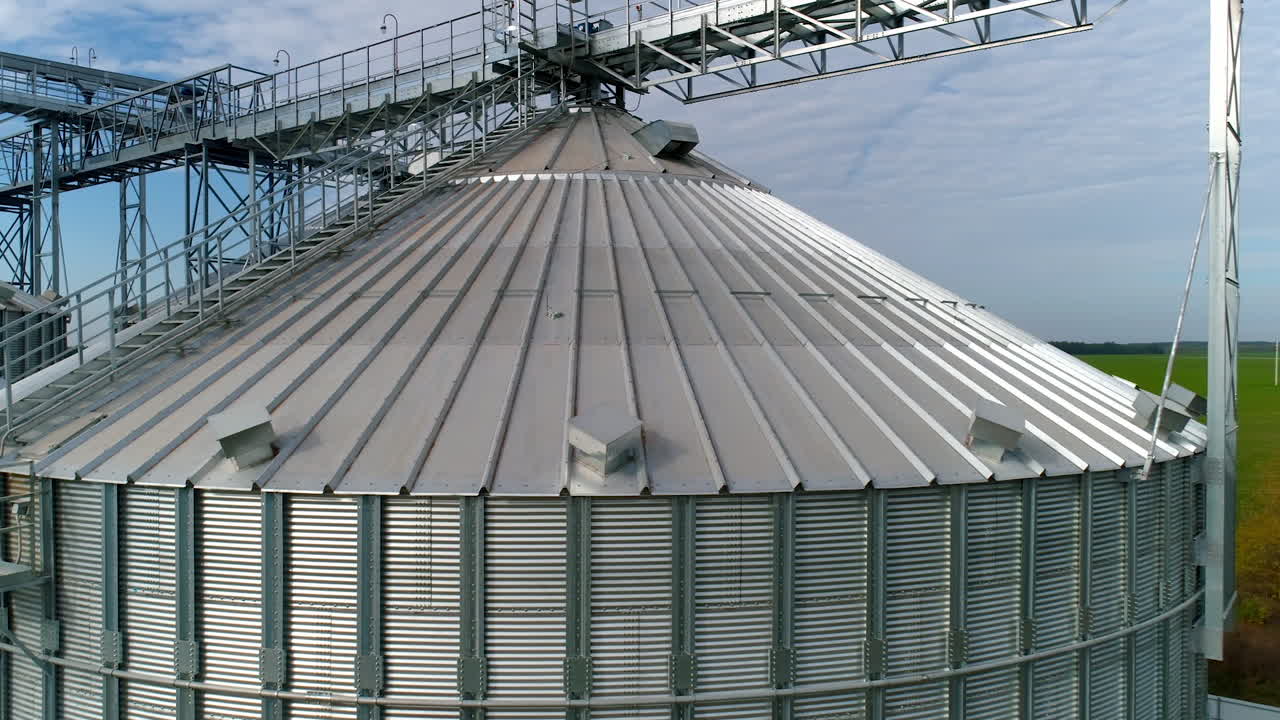 Modern plant for agribusiness. Large grain terminals on nature background. Silver grain elevators. Aerial view. Camera moves around.
