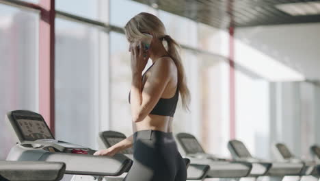 Slim-sport-woman-talking-mobile-phone-in-fitness-gym.-Fit-girl-walking-treadmill