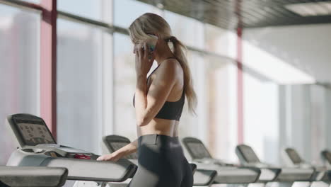 Mujer-Deportiva-Delgada-Hablando-Por-Teléfono-Móvil-En-El-Gimnasio.-Chica-En-Forma-Caminando-En-Cinta-Rodante