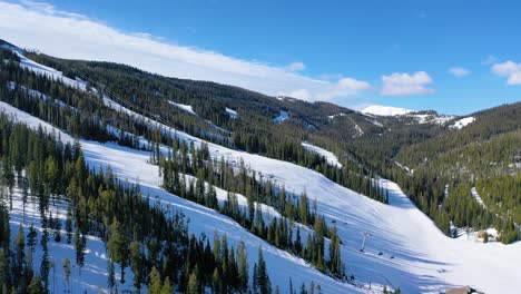 chair lifts float over fresh powder and skiers in motion in this aerial of big sky, montana’s popular ski resort, surrounded by frosty trees and towering snow-capped peaks