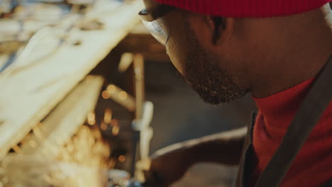 black craftsman shaping steel billet with grinder in blacksmith workshop