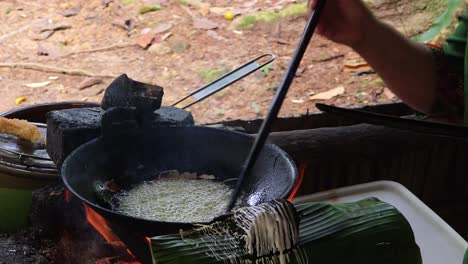hands expertly pour batter to create threads of traditional kuih jala (jala emas) snack, frying over fire on a banana leaf at mari mari village in malaysia