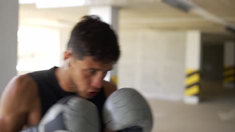 the man executes strong blows in the boxing bag at the parking zone gym, close up