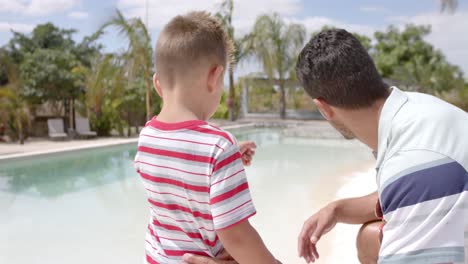 padre y hijo caucásicos felices hablando en la piscina de la casa de la playa