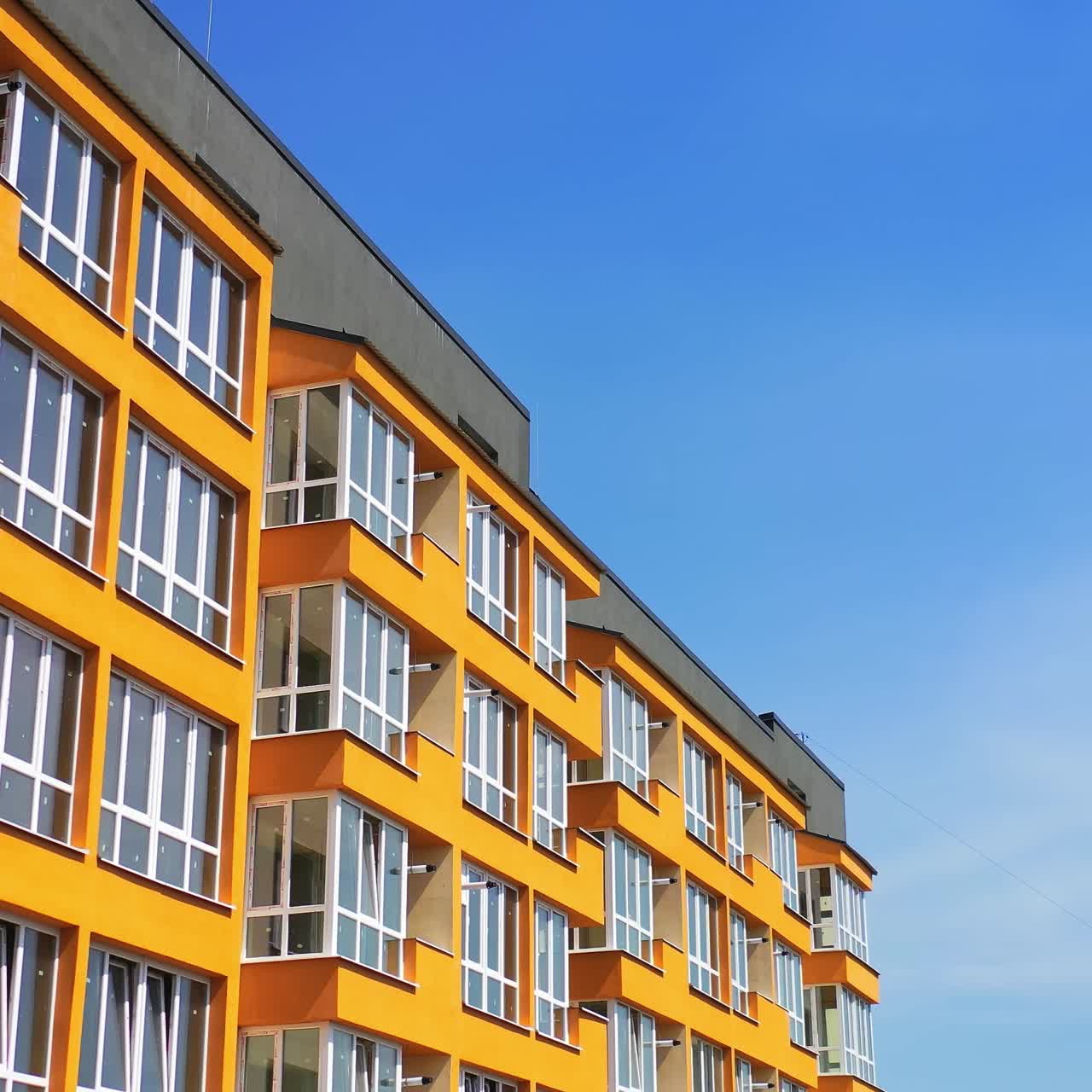 Bright city architecture against blue sky. New apartment building in orange color for urban residents. Modern design of high-rise building