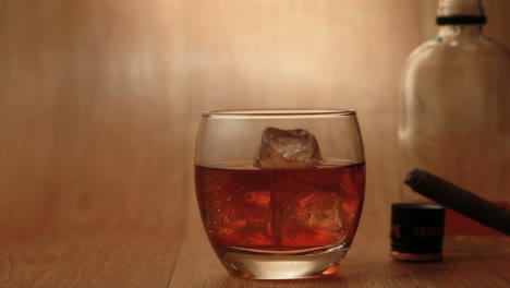 cigarro siendo fumado al lado de un vaso de whisky en las rocas