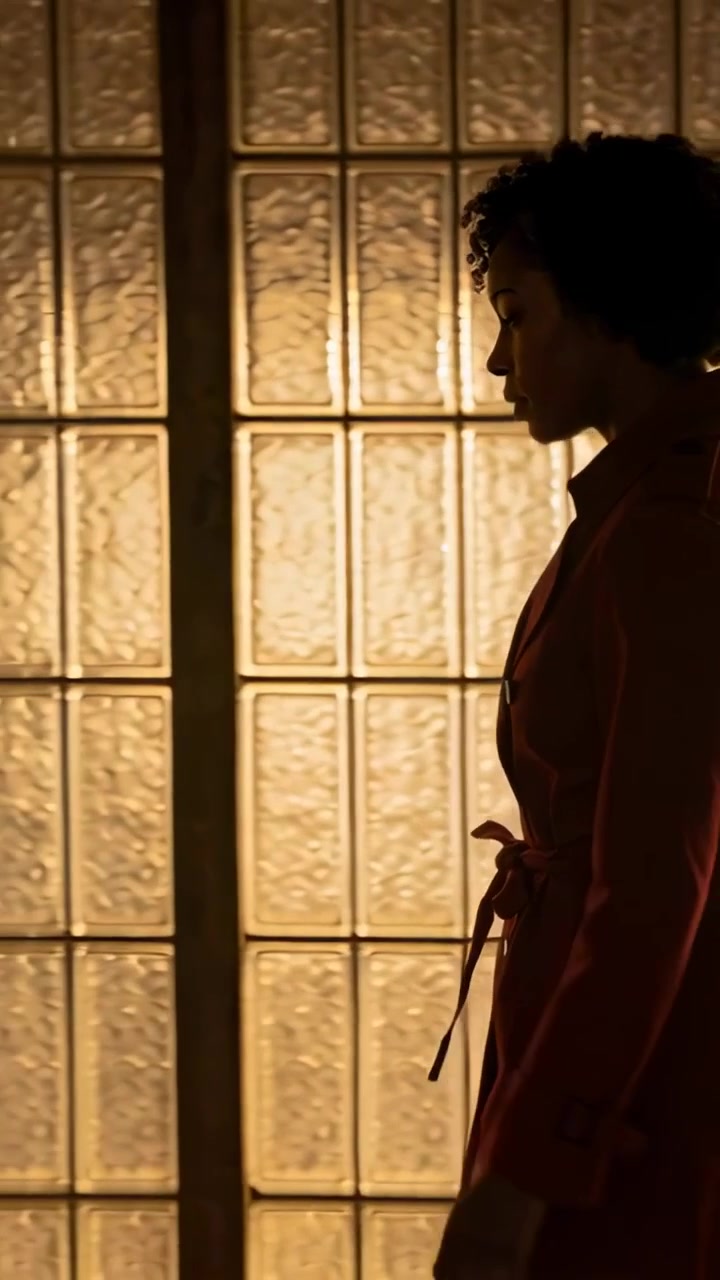 Vertical video: Entering right woman walking left along hall glass wall in belted coat, copy space