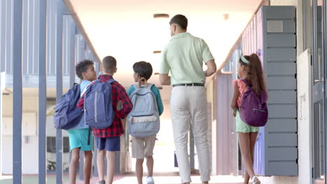 Young-Asian-man-walks-with-diverse-students-at-school,-with-copy-space