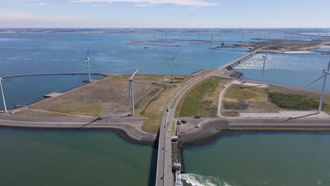 Aerial-wide-angle-pull-back-shot-of-multiple-active-wind-turbines-standing-behind-the-eastern-Scheldt-Storm-Surge-Barrier-in-Zeeland,-Netherlands