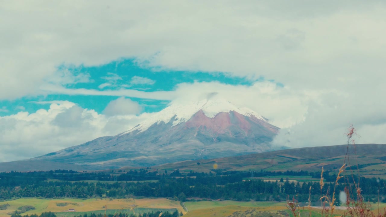 Una vista del vulcano Cotopaxi con la vetta innevata e roccia vulcanica rossa sotto un cielo nuvoloso in Ecuador