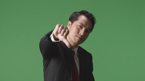 아시아 사업가 는 그린 스크린 스튜디오 에 서 있는 동안 엄지손가락 을 내려 놓은 몸짓 을 하고 있다