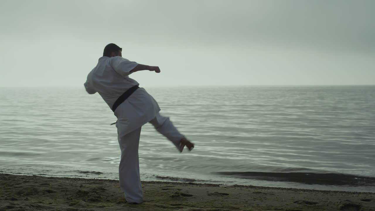 deportista barbudo practicando el ataque al atardecer al aire libre. hombre de karate aprendiendo patadas