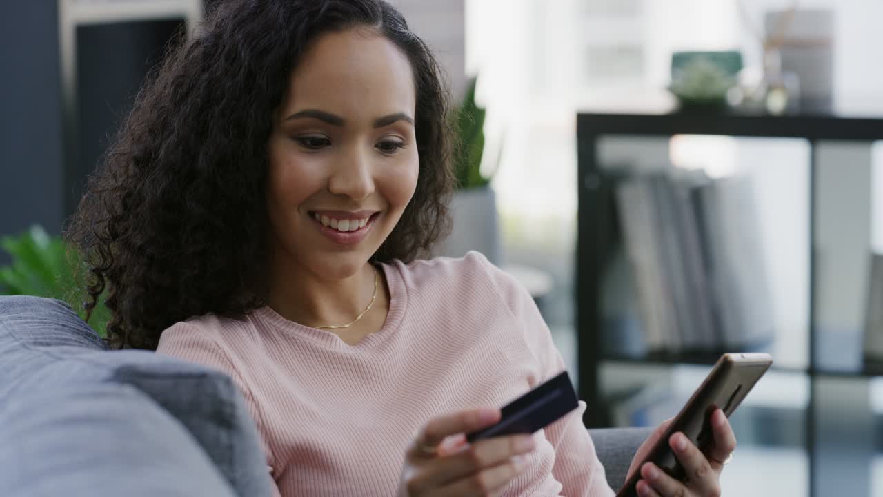 imágenes de video en 4k de una mujer joven sentada en su sofá en casa y usando su teléfono celular para comprar en línea