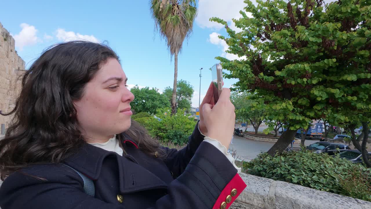 Woman Taking a Photo in a City Park near an Ancient Wall
