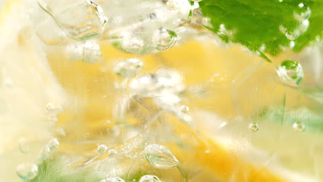 lemonade in a glass - air bubbles squeeze between the lemon slices, ice and mint in macro and slow motion