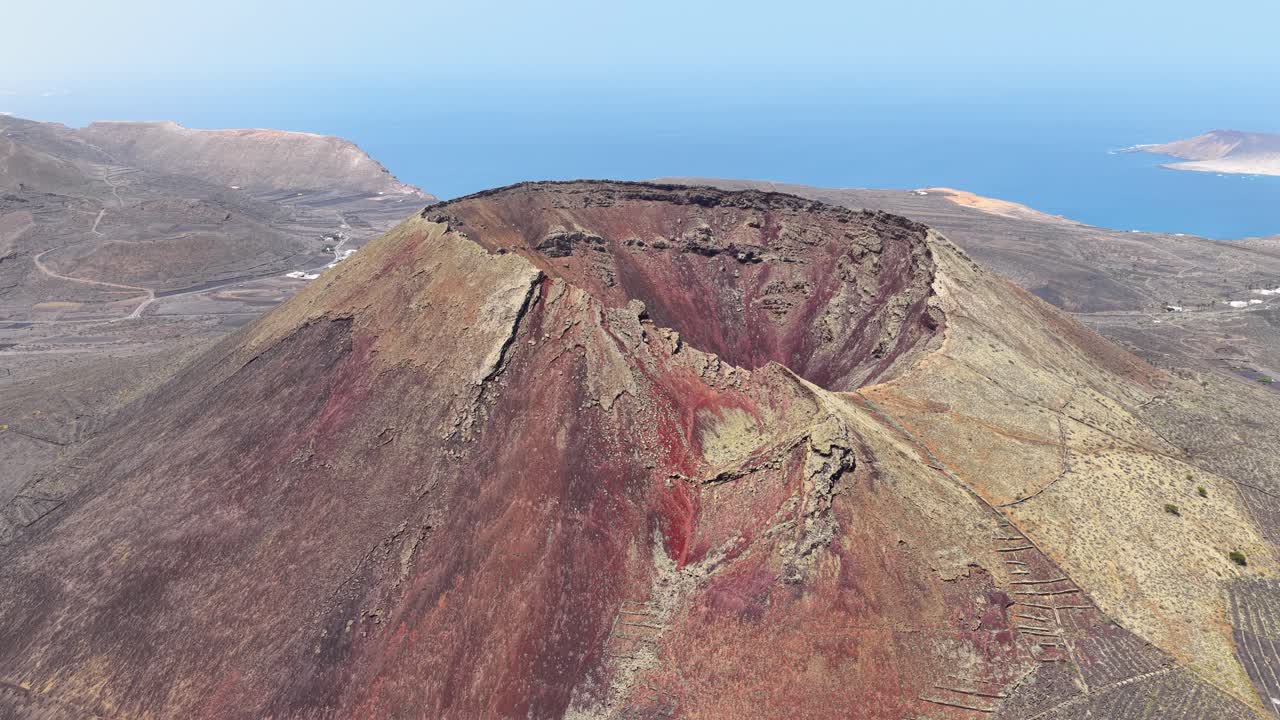 Aerial View Of Volcan de la Corona Crater Overlooking Volcanic Terrain And Atlantic Ocean In Lanzarote, Spain. ascending tilt-down shot