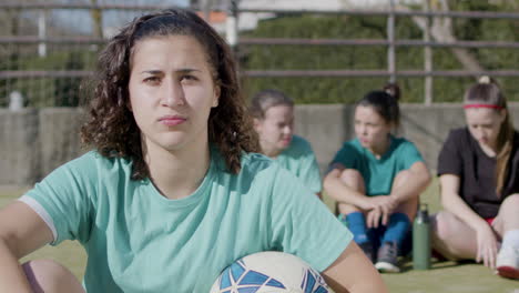 sporty teenaged girl looking at camera, while her teammates relax behind