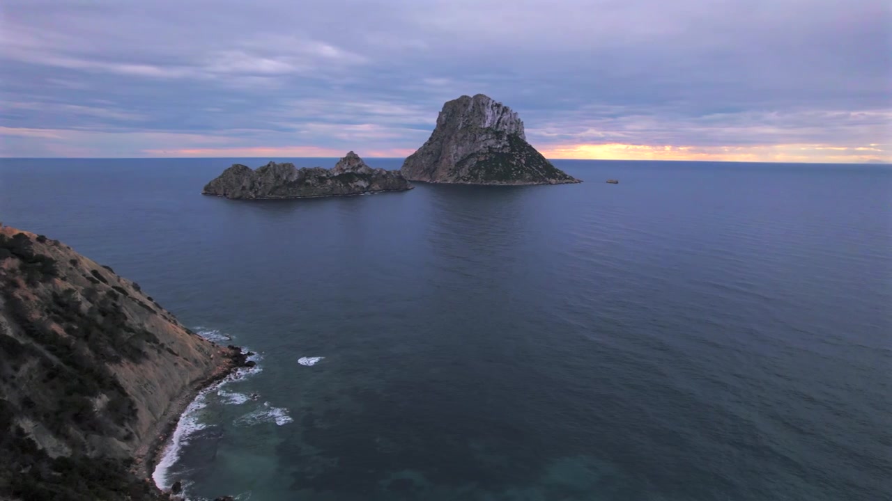 Ripresa aerea in 4K con drone di Es Vedrà al tramonto, Ibiza, Spagna. L'iconica isola rocciosa emerge dal Mar Mediterraneo mentre una calda luce dorata illumina la costa e le acque circostanti