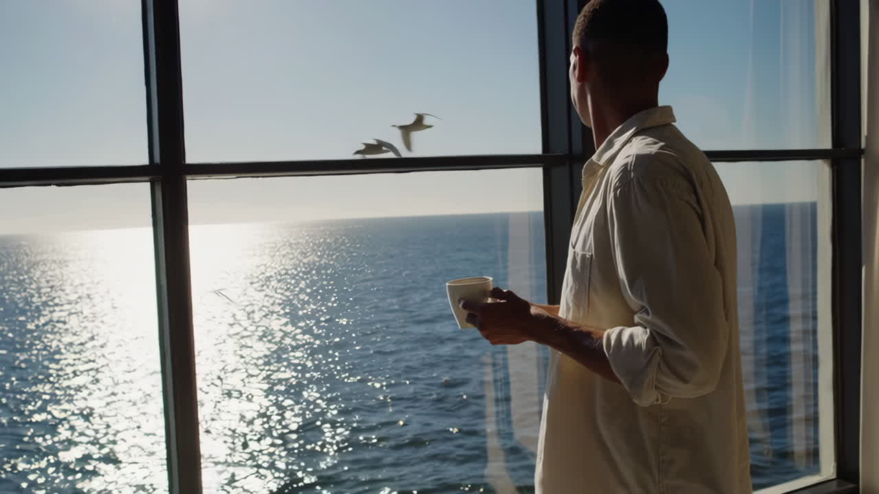Man drinking coffee and contemplating by the ocean view window