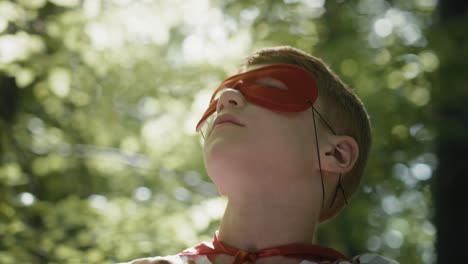 ginger caucasian boy with superhero costume looking on in forest.