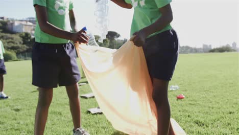 Fröhliche,-Vielfältige-Schulkinder-Tragen-Recycling-T-Shirts-Und-Reinigen-Den-Sportplatz-In-Der-Grundschule