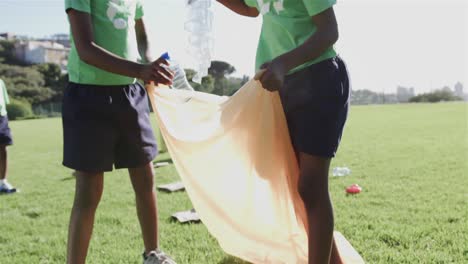 escolares felices y diversos usando camisetas recicladas limpiando el campo de deportes en la escuela primaria