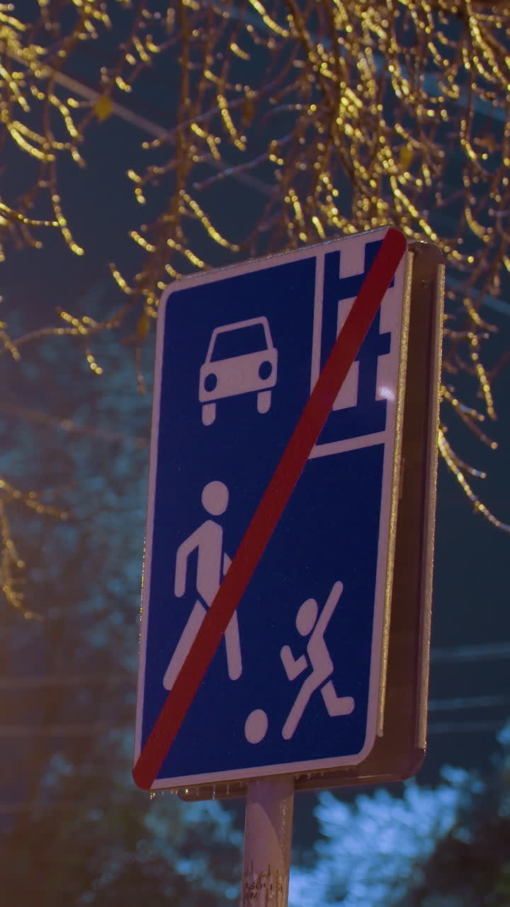 señal de tráfico debajo de las ramas de los árboles con luz brillante en el fondo durante el anochecer. iluminado por la luz de la calle amarilla cálida, rodeado de ramas desnudas que reflejan la luz