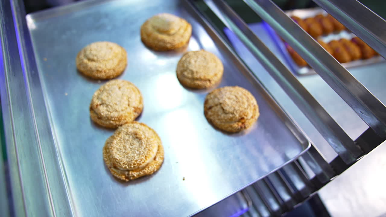 Sweet pastry manufacturing at bakery. Brown baked bagels and buns put on the baking sheet. Close up.