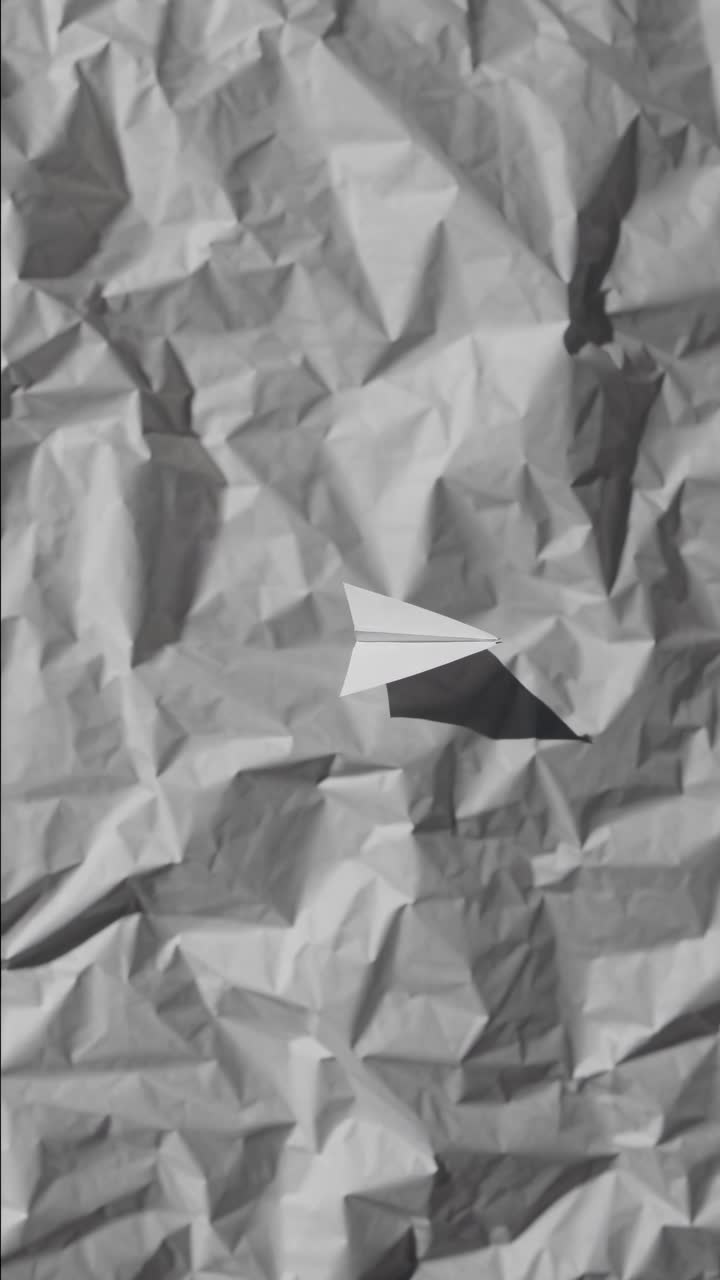 Aerial view of a paper airplane on crumpled paper, creating a playful, minimalist style
