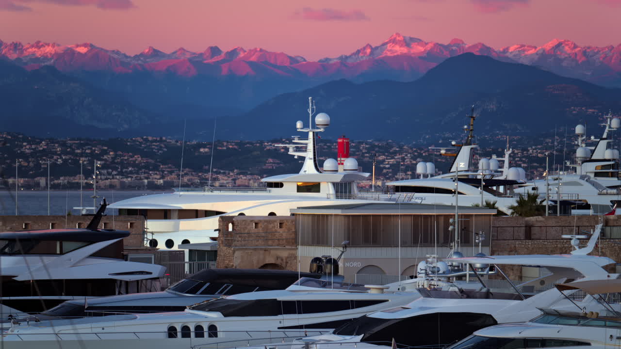 Juan-les-Pins, France - January 25, 2025: Multiple white boats docked in the harbour in Antibes with the mountains on the background at sunset