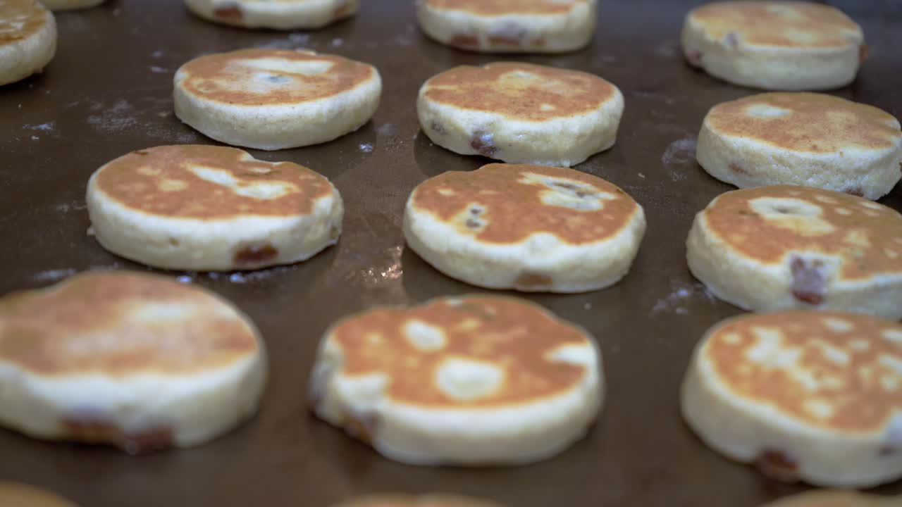Kue Welsh dibalik di atas wajan datar. Warna hangat makanan tradisional. Gerakan kamera panoramik lambat.
