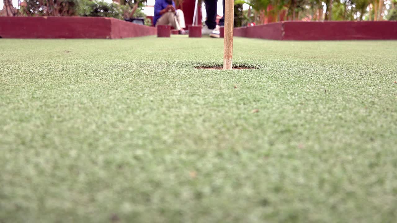 Close and Low Shot of a Golf Ball Being Putted into the Hole at Mini Golf