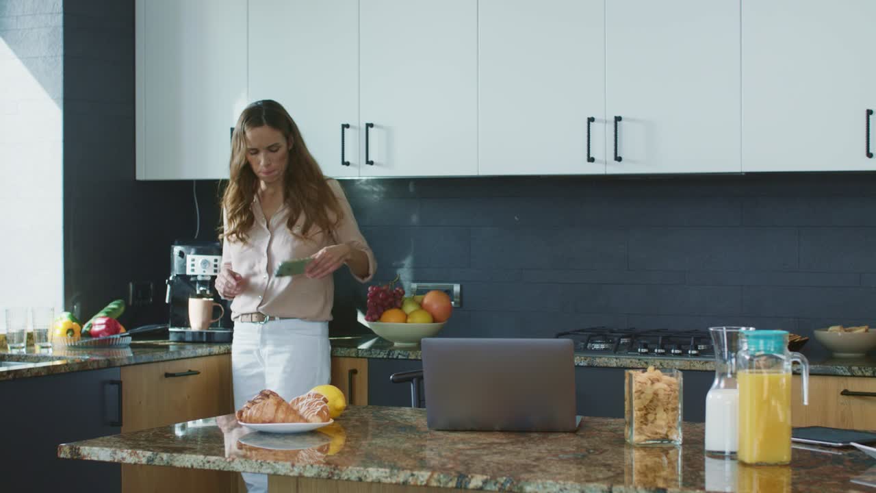 Donna d'affari che prepara il caffè in cucina. Persona rilassata che controlla il telefono cellulare.