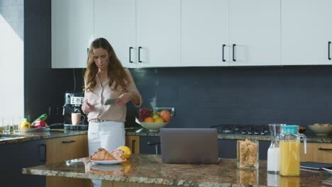 Business-woman-preparing-coffee-in-kitchen.-Relaxed-person-checking-mobile-phone