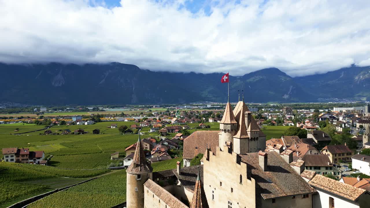Pull out drone shot close to beautiful Aigle Castle in Vaud Switzerland with Swiss flag waving