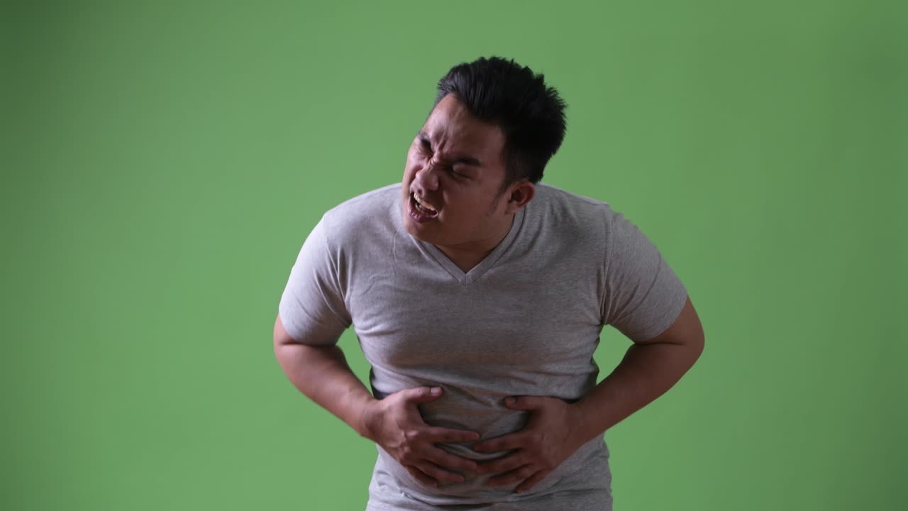 Young handsome overweight Asian man against green background