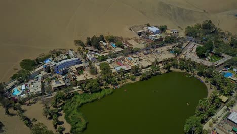 aerial shot over huacachina oasis lake surrounded by sand dunes in atacama desert, peru