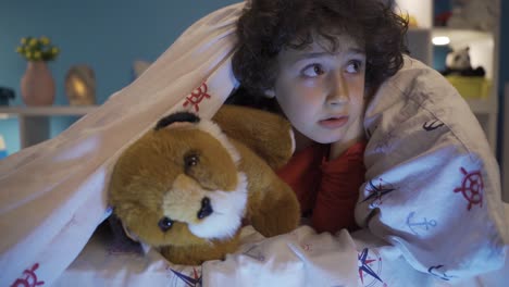 un niño lindo escondiéndose debajo de la cama con su perro de juguete, jugando.