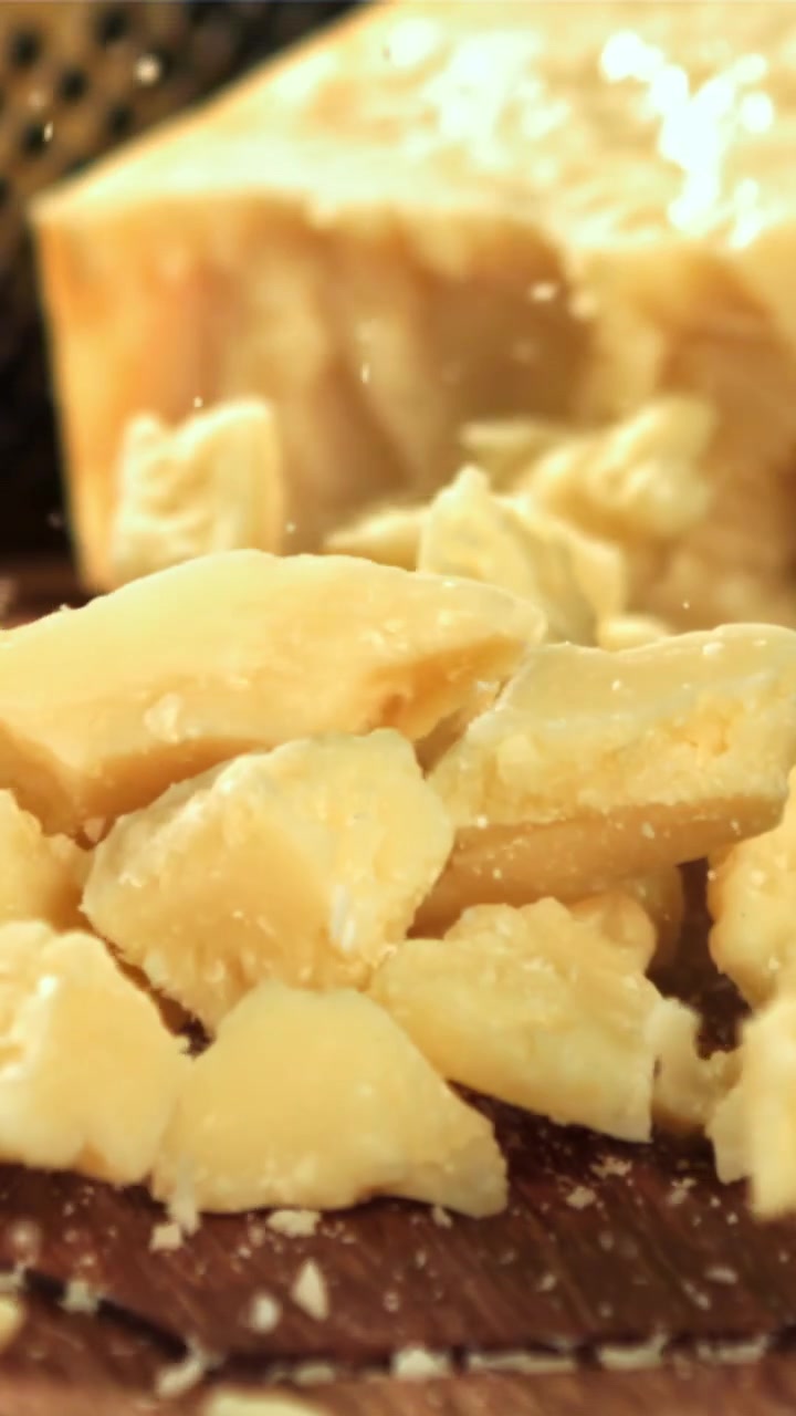 Slow Motion Close-Up of Parmesan Cheese Pieces Falling onto a Wooden Board