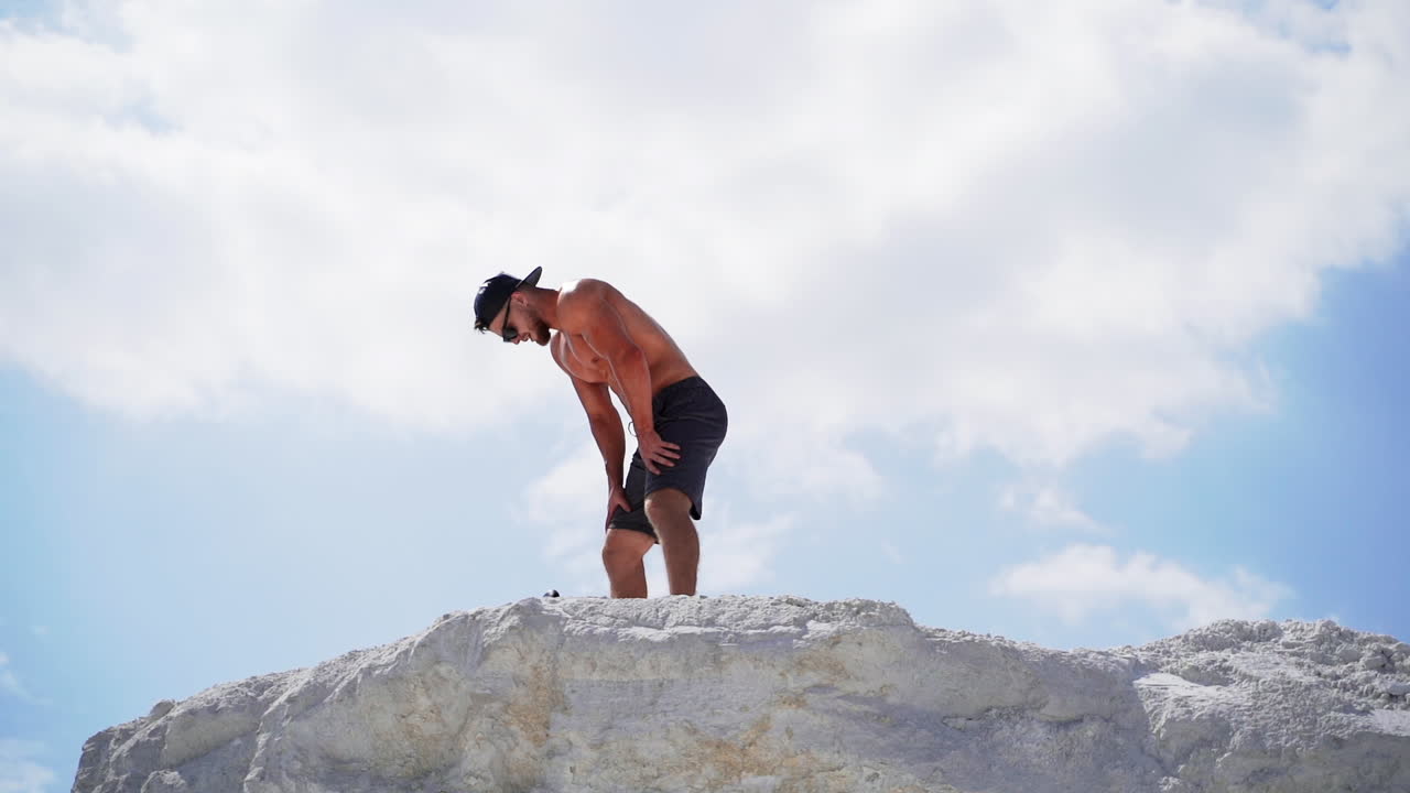 Young man contemplating after training. Young sportive male resting on top of mountain