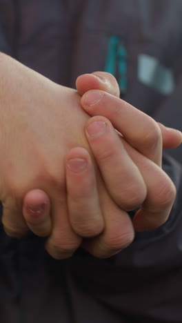 primer plano de las manos juntas en un giro pensativo o un gesto contemplativo, con enfoque en los detalles de la piel y la chaqueta de invierno