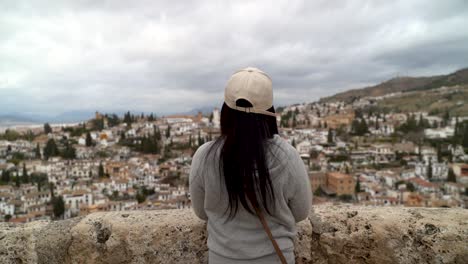 Dolly-in-towards-girl-standing-on-lookout-over-cityscape