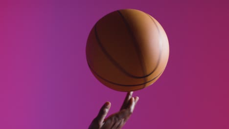 close up studio shot of male basketball player spinning ball on finger against pink lit background 2